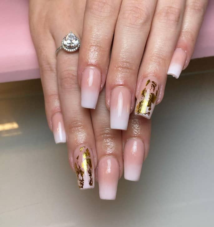 A closeup of a woman's fingernails with nude-to-white ombré nail polish that has gold foil flakes on the accent nails