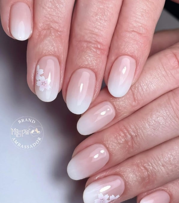 A closeup of a woman's fingernails with a beige ombré nail polish that has white flowers on select nails 