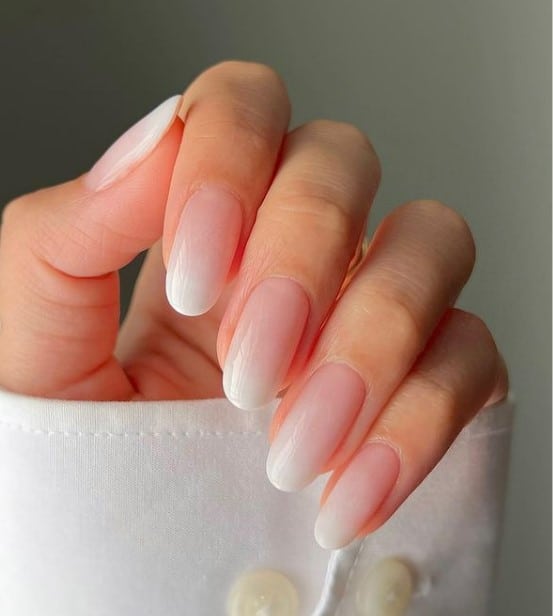 A closeup of a woman's oval fingernails with nude ombré nails