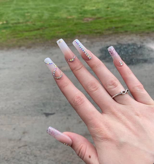 A woman's fingernails with almost clear beige ombré nail polish that has tiny rhinestones with iridescent color arranged in different ways