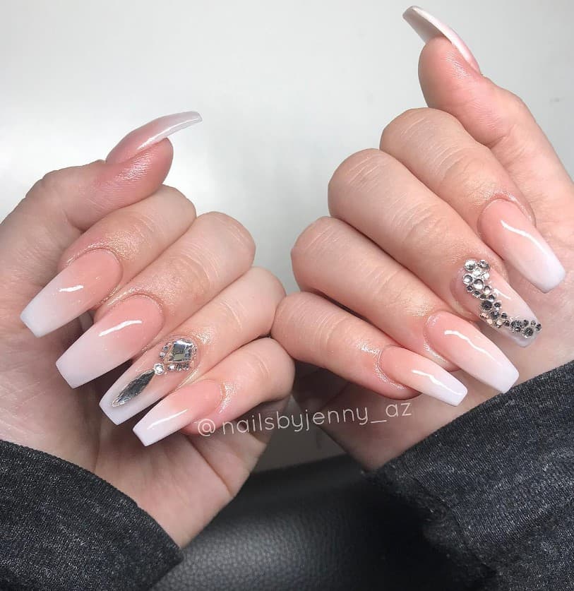 A closeup of a woman's fingernails with a peach beige ombré nail polish that has large silver crystals on select nails 