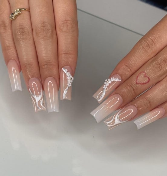 A woman's fingernails with sheer white blends with the beige base that has white and silver swirls and tiny white flowers