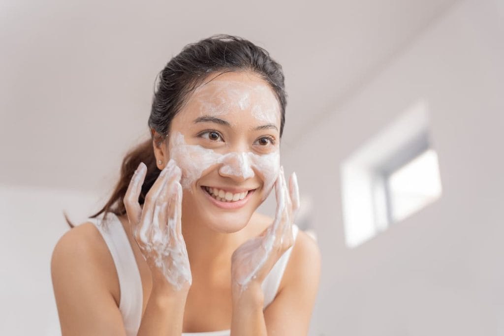 Asian woman applying facial washto her face.