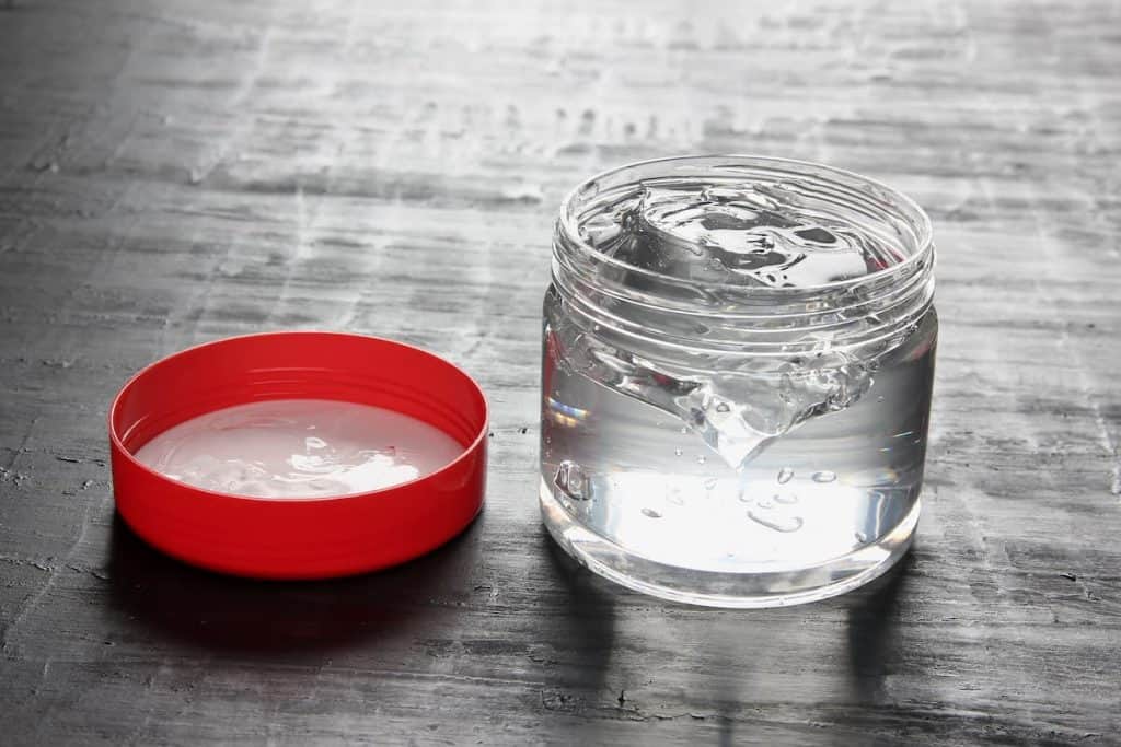 A jar of hair gel next to a red cap.