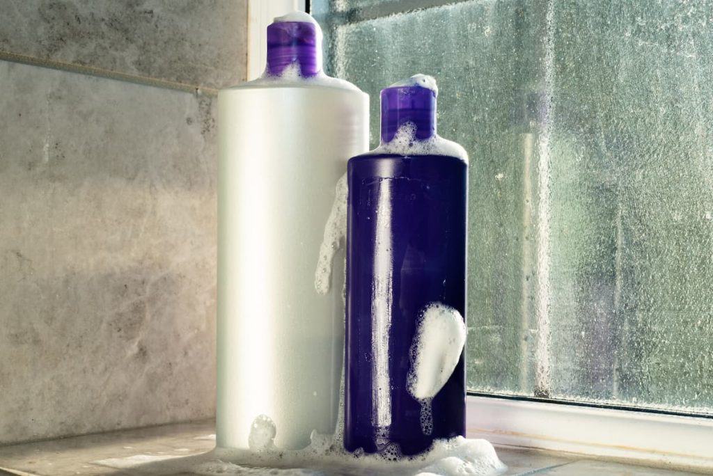 Two bottles of purple shampoo sitting on a window sill.