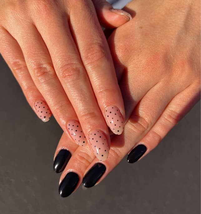 A closeup of a woman's black and nude fingernails with glossy black nails on the left hand and sheer nude that has dainty black dots on the right hand