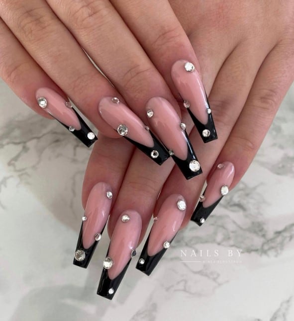 A closeup of a woman's fingernails with long, perfectly sculpted coffin nails that has deep French tips and jeweled rhinestone accents