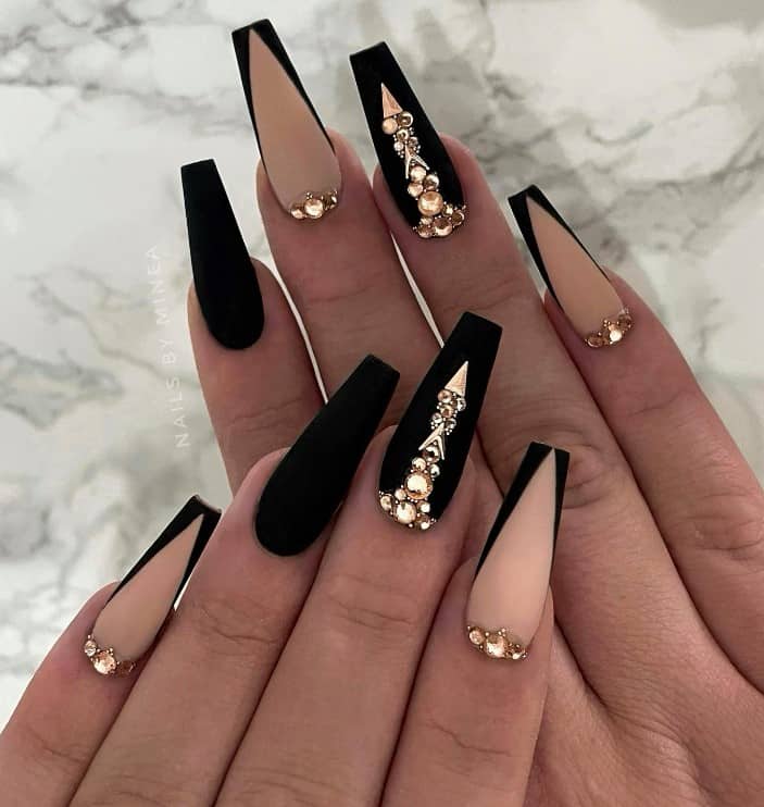 A closeup of a woman's fingernails with black and nude matte mani that has sparkly gold accents and deep chevron tips on select nails