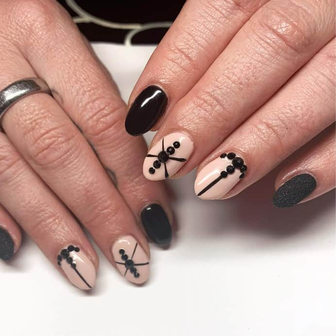A closeup of a woman's fingernails with Glossy black nails and nails with sugary black glitter that has shiny nude nails with black crystals and lines