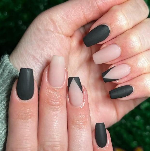 A closeup of a woman's fingernails with matte black and nude nails that has V-shaped French tips on the nude accent nails