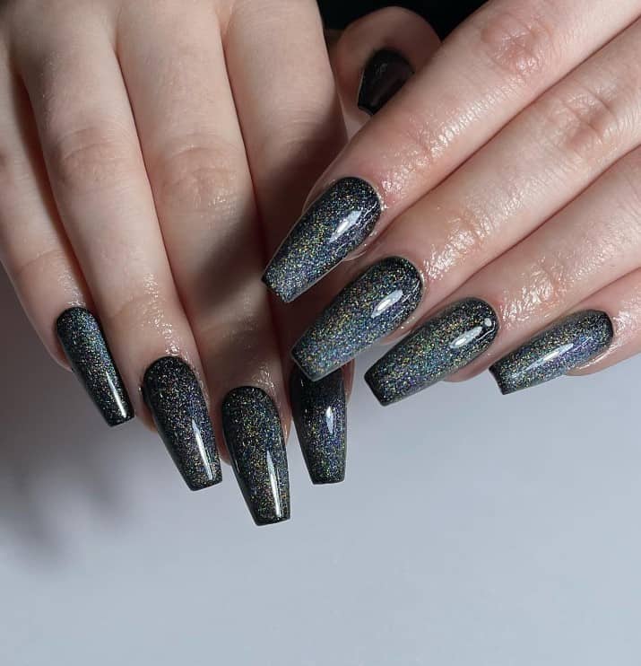 A closeup of a woman's fingernails with a black nail polish that has glitter