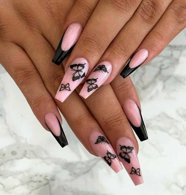 A woman's fingernails with a nude nail polish base that has plain black French tips and butterfly nail art