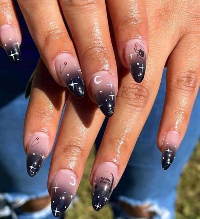 A closeup of a woman's fingernails with a black-tip ombré nails that has moon, star, spiderweb, and safety pin nail stickers 