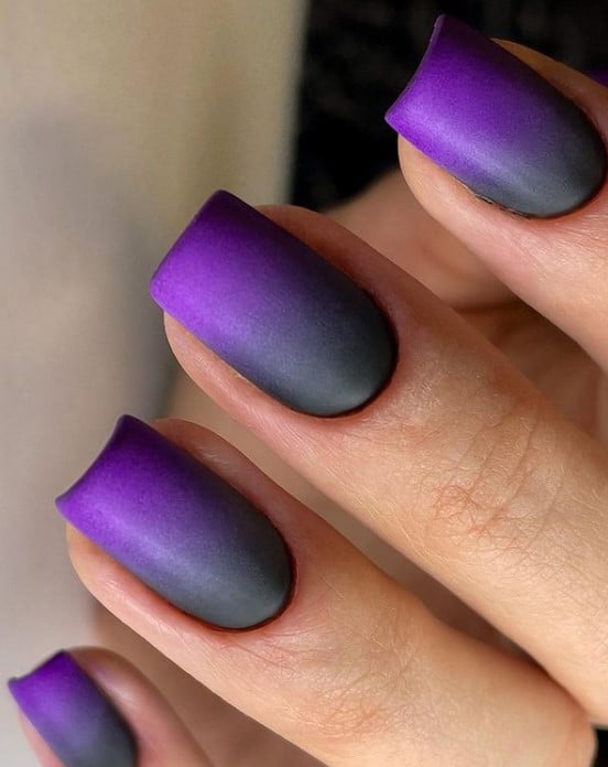 A closeup of a woman's fingernail with eye-catching purple-and-black ombré nails in a square shape that has matte finish for a chic and fabulous mani