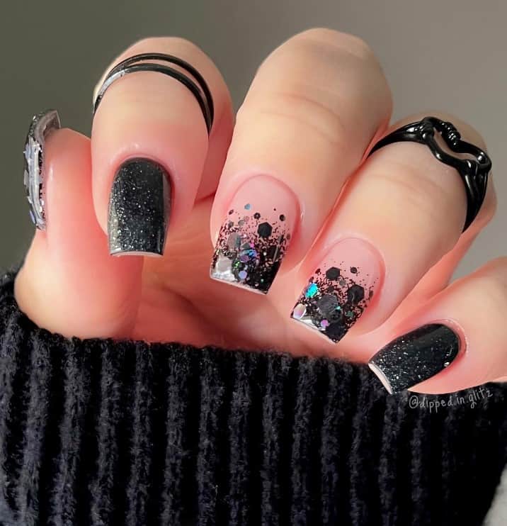 A closeup of a woman's fingernails with a mix of nude and black nail polish that has gorgeous ombré effect using chunky black glitter flakes
