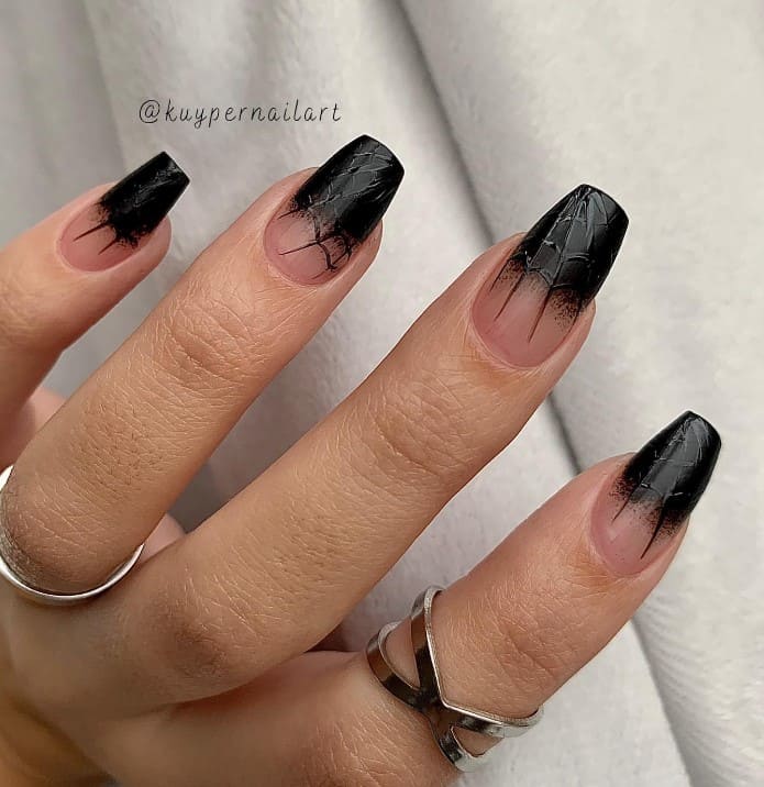 A closeup of a woman's fingernails with clear-to-black ombré nails that has spiderweb nail art with a matte finish