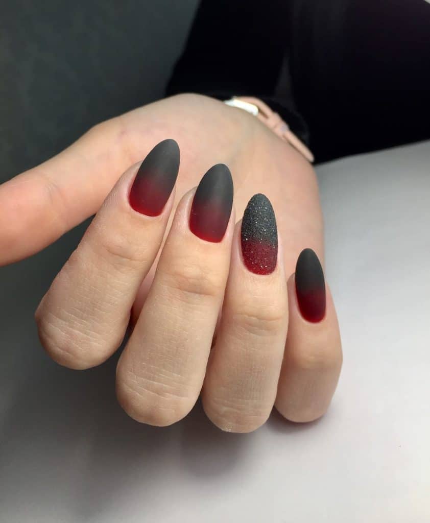A woman's fingernails with black-and red-ombré nails that has a fine sugar-textured accent nail