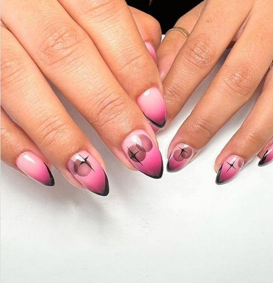A closeup of a woman's fingernails with pink-and-black ombré nails that has star and bubble nail art