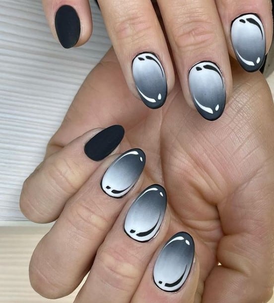 A closeup of a woman's fingernails with matte black ombré nails that has monochromatic black palette and matte black accent nails