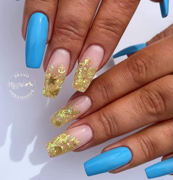 A closeup of a woman's fingernails with sky-blue nails and peach-colored accent nails that has chunky gold dust and sequins shaped like clams, starfish, and seahorses nail tips