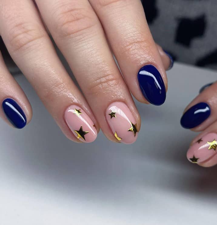 A woman's fingernails with navy blue shade and pinky peach hue accent nail that has gold stars on select nails