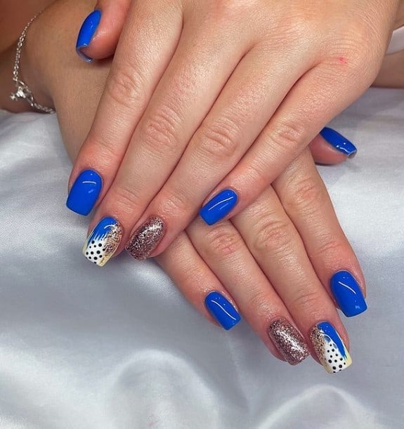 A woman's fingernails with a royal blue and a rose gold glitter nail polish that has multicolored abstract tips on select nails 