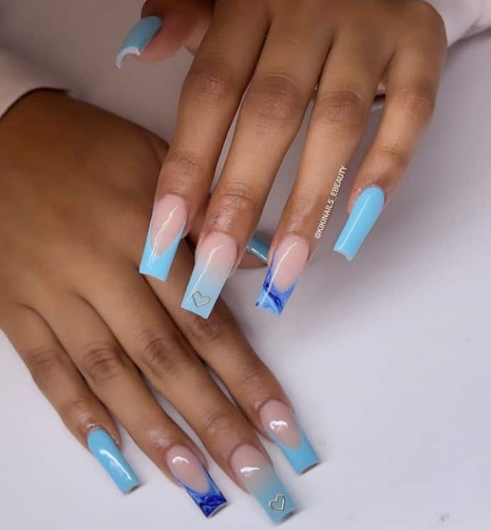 A woman's fingernails with a combination of nude and baby blue nail polish that has tiny silver hearts on tips
