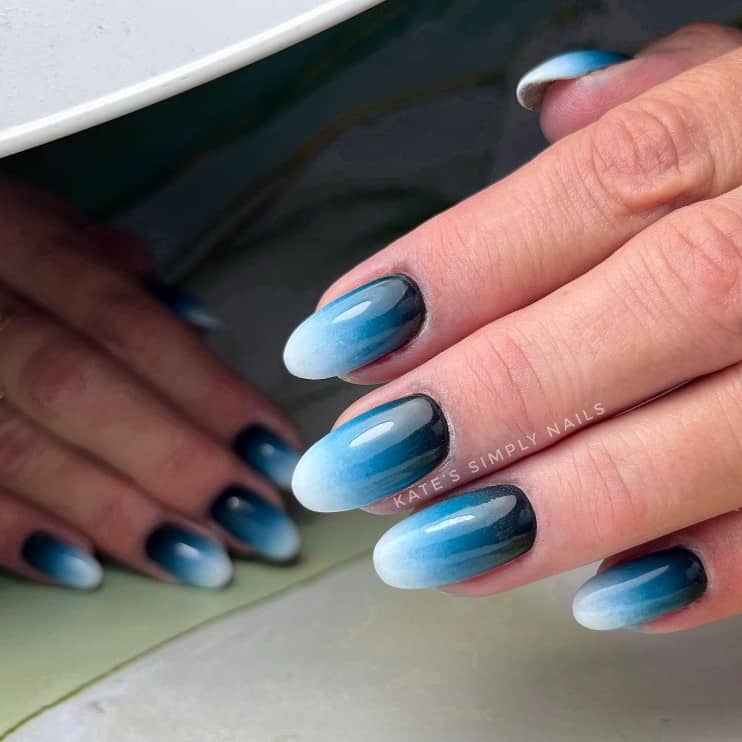 A closeup of a woman's fingernails with white, blue, and black ombré nail polish 