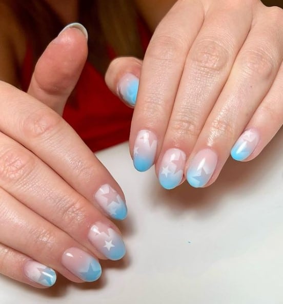 A woman's fingernails with baby blue ombré nail polish that has stars nail designs