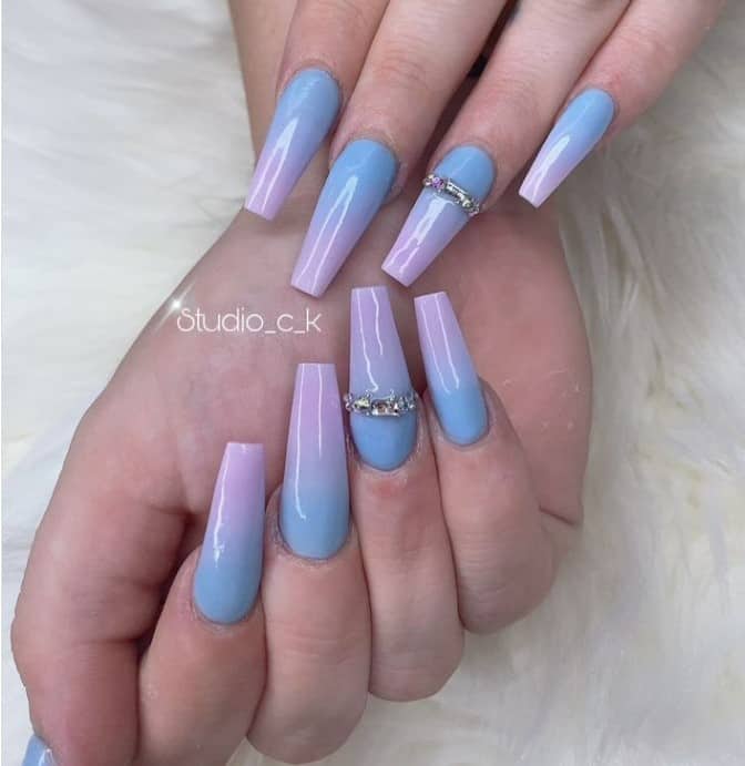 A closeup of a woman's fingernails with lavender-and-blue ombré nail polish that has jewel accents