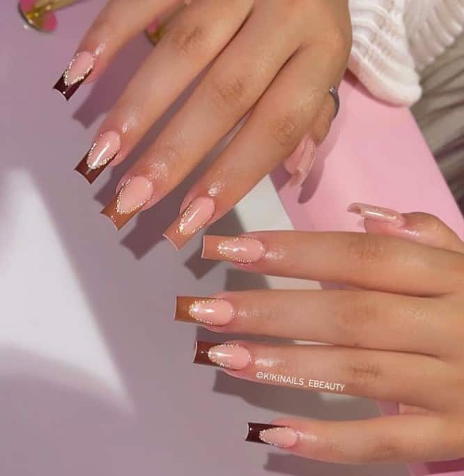 A closeup of a woman's fingernails with a nude nail polish that has tips with different shades of brown and a silver glitter outline to each nail
