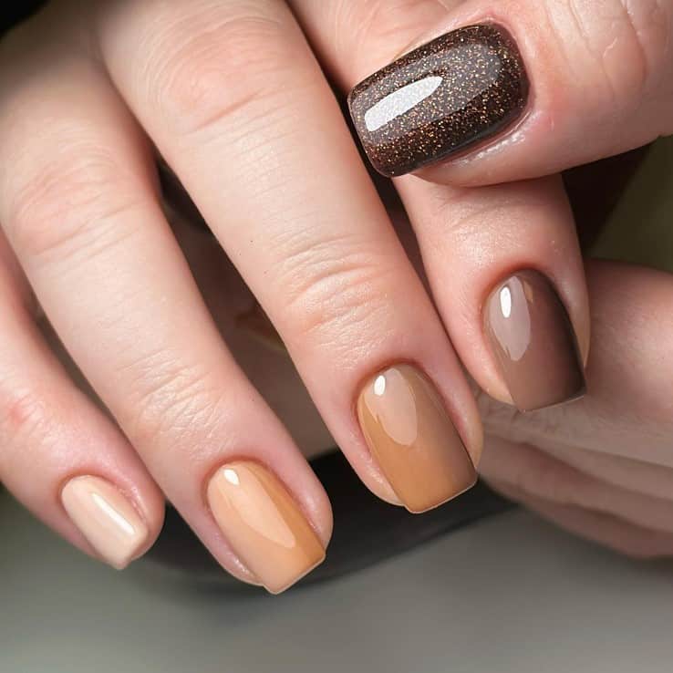 A closeup of a woman's fingernails with a glossy different shades of brown nail polish that has deep brown glitter