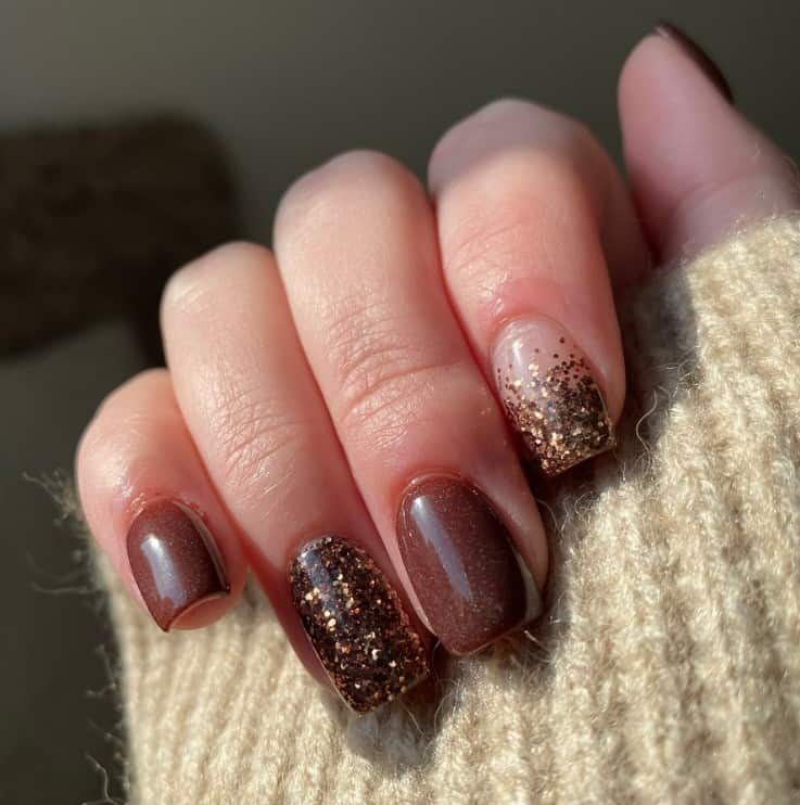 A closeup of a woman's fingernails with brown glitter, chunky brown and gold glitter nail polish