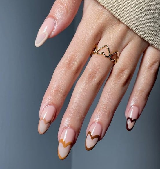 A woman's  fingernails with a nude nail polish base that has different shades of brown polish in heart-shaped French tips