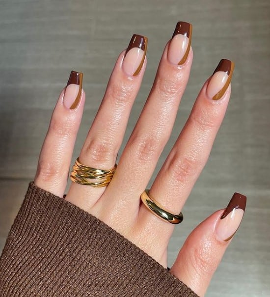 A woman's fingernails with a glossy nude nail polish that has a swoopy leather brown line to one side of each nail