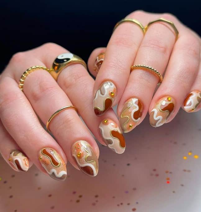 A closeup of a woman's fingernails with a combination of different shades of brown that has yellow rhinestones and gold outlines