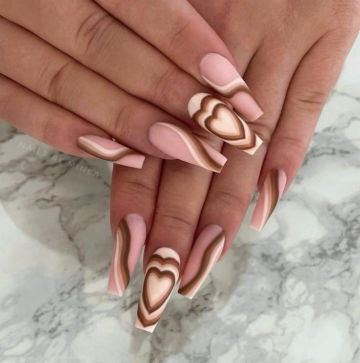 A closeup of a woman's fingernails with a nude nail polish that has four shades of brown in different designs such as swirls, diagonal lines, and heart accents
