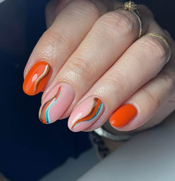 A woman's fingernails with a combination of sheer peach and burnt orange nails that has multicolored streaks in orange, brown, gold, white, and turquoise on the sheer peach base and streaks in brown, white, and gold on burnt orange-colored nail