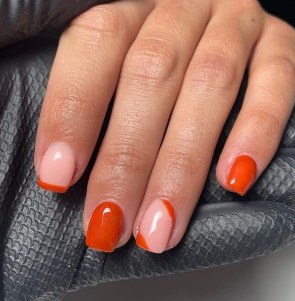 A closeup of a woman's fingernails with a combination of nude and burnt orange nail polish base that has French tips, and diagonal burnt orange lines on the tips and cuticles