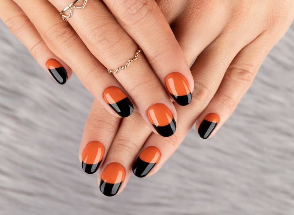 A woman's fingernails with a glossy burnt orange nail polish base that has black nail tips 