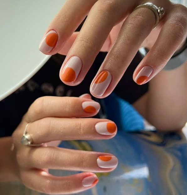 A woman's short fingernails with a white nail polish base that has irregularly-shaped circles in burnt orange