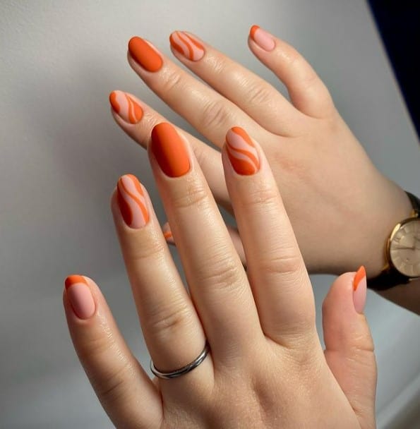 A closeup of a woman's fingernails with a combination of soft peach and burnt orange nails that has peach-colored streaks and burnt orange French tips on a soft peach base