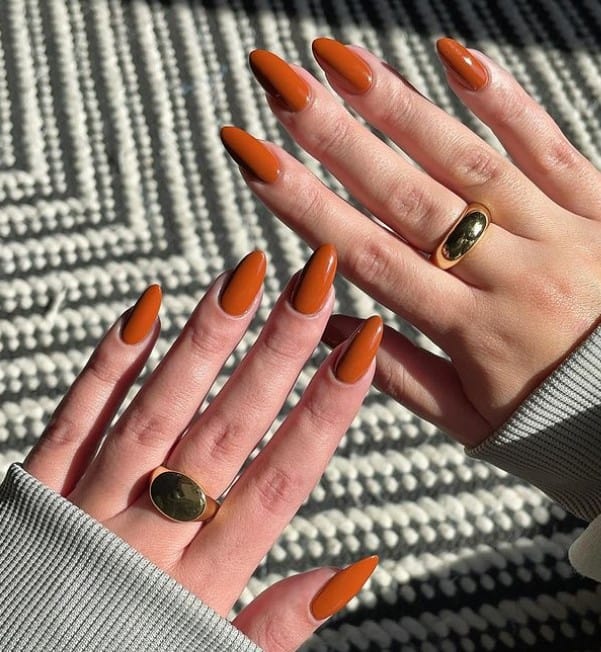 A woman's long fingernails with a burnt orange nails 