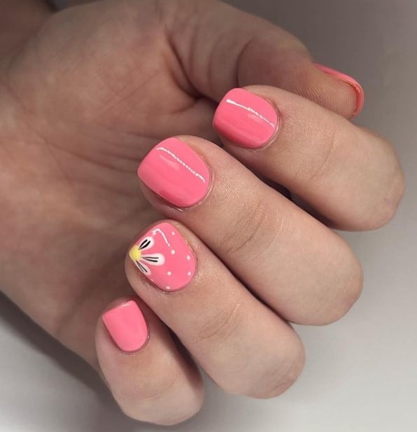 A closeup of a woman's fingernails with salmon pink nail polish that has black-and-white daisy on select nails