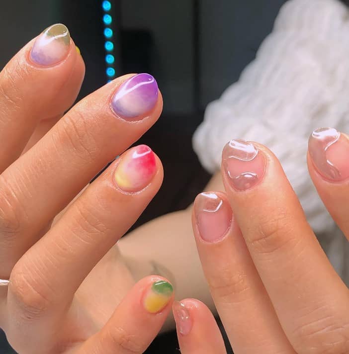 A closeup of a woman's fingernails with different gel nail color that has a marble effect and jelly-glazed nails