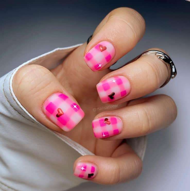 A closeup of a woman's fingernails with a nude nail polish that has bright pink gingham patterns, heart and star accents