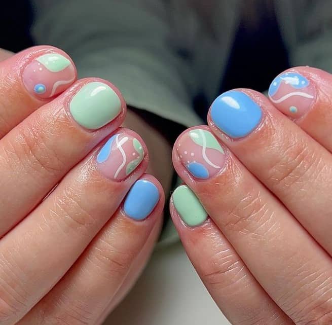 A closeup of a woman's fingernails with a combination of soft blue and green nail polish that has abstract nail art on select nails
