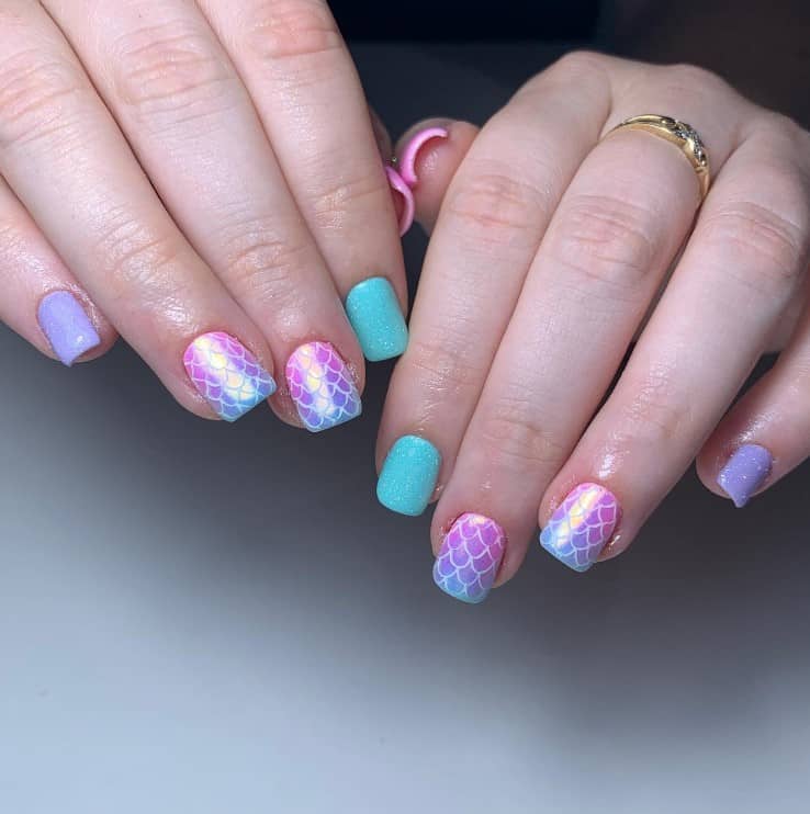 A woman's fingernails with a combination of blue and purple nail polish that has iridescent mermaid scales nail designs on select nails