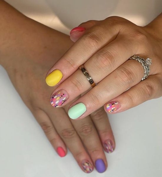 A woman's fingernails with a combination of yellow and green pastel nail polish that has tiny pink, white, black, and lavender abstract spots