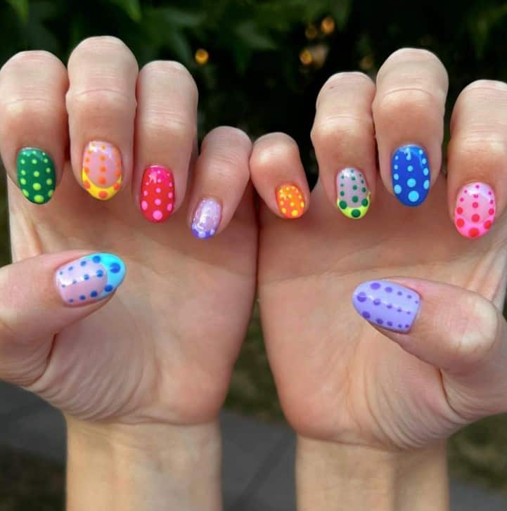 A closeup of a woman's fingernails with polka dots that has bright and vibrant colors